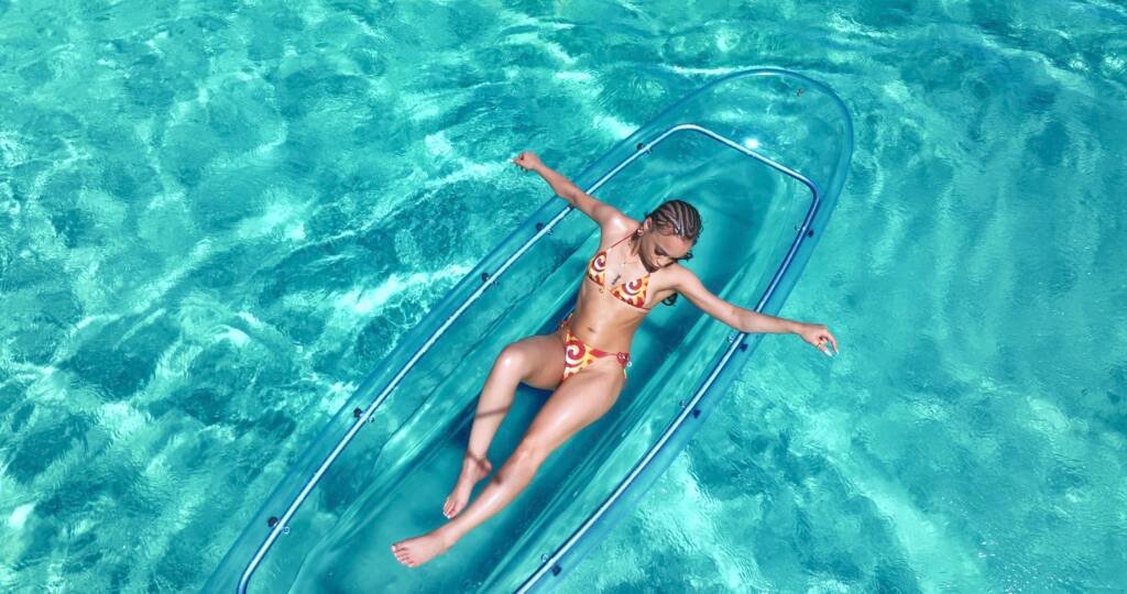 Drone shot: woman relaxing with arms out in a clear kayak in Aruba