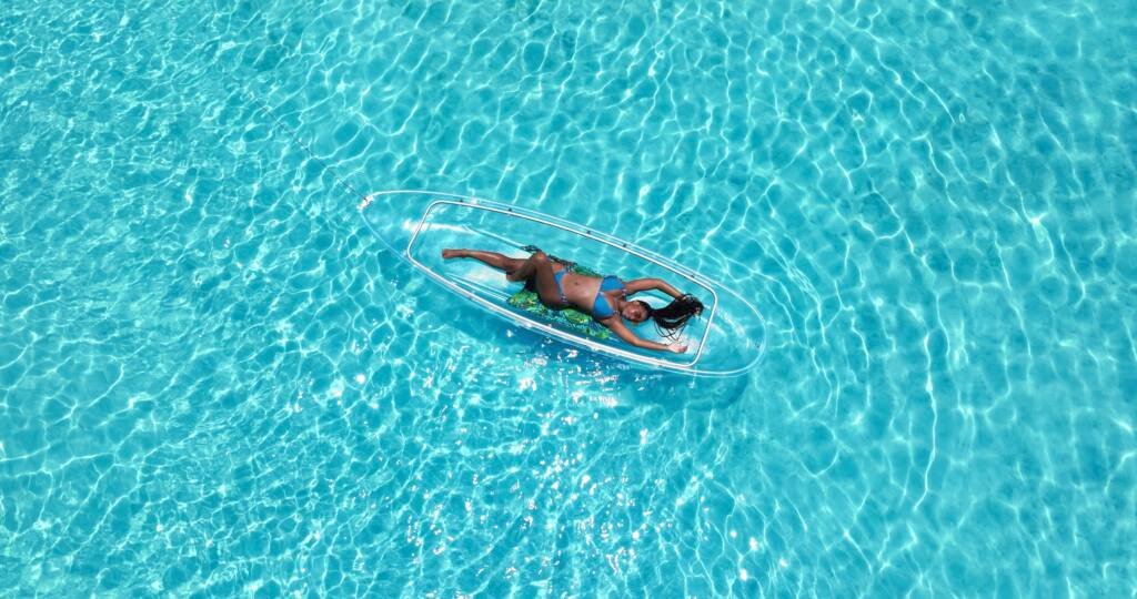 Drone shot: person lying in a clear kayak on open turquoise water in Aruba