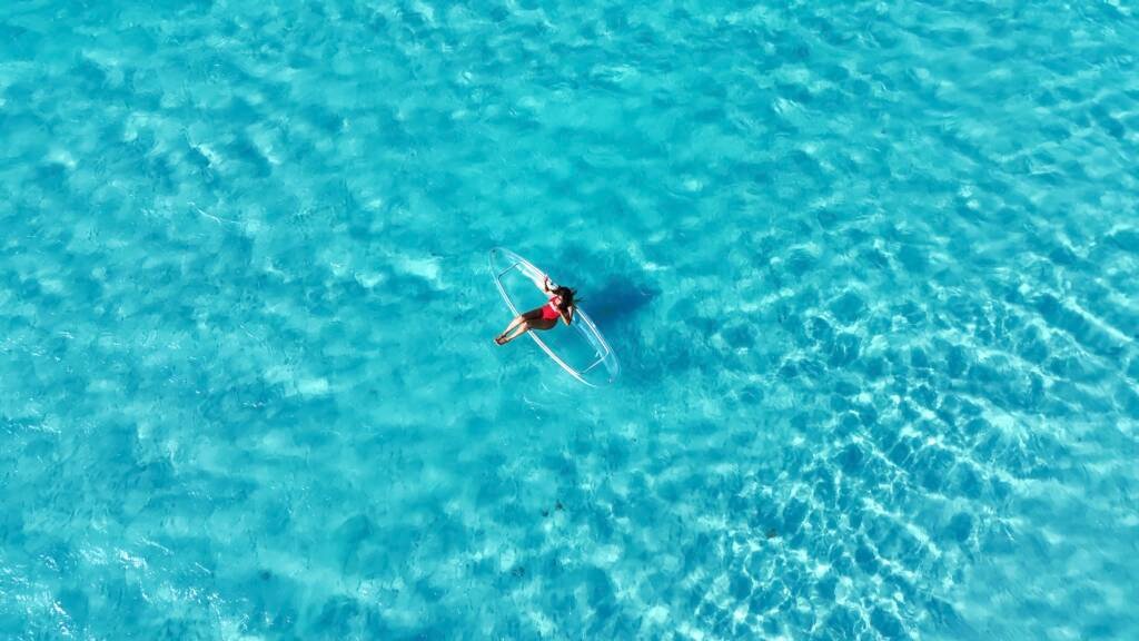 Drone shot: small clear kayak on wide open turquoise water in Aruba
