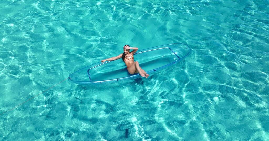 Drone shot: woman sitting on a clear kayak on turquoise water in Aruba