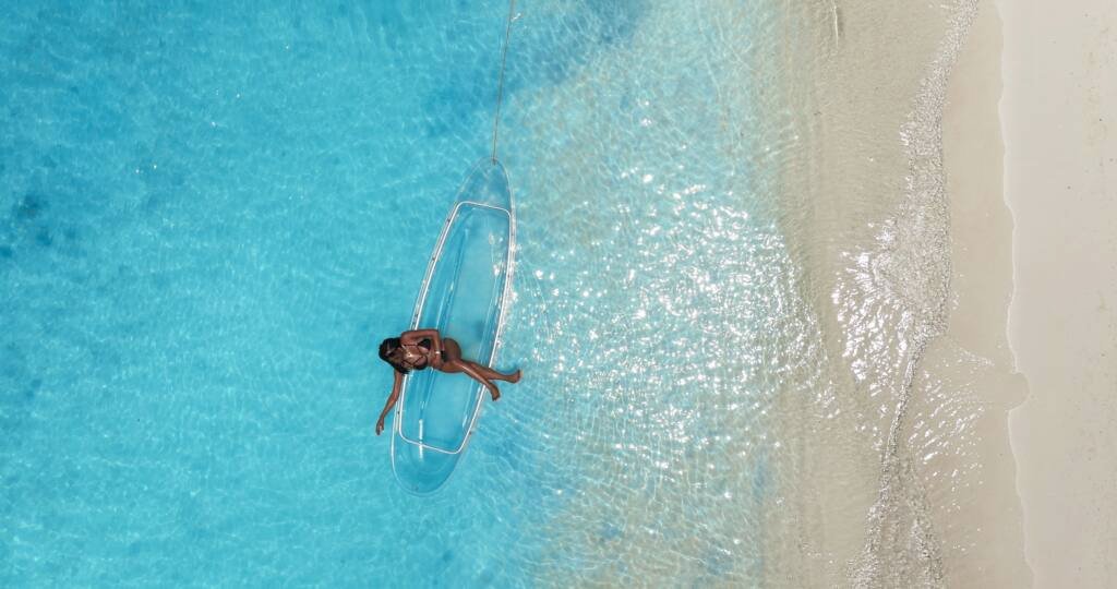 Drone shot: clear kayak floating beside a white sand beach in Aruba